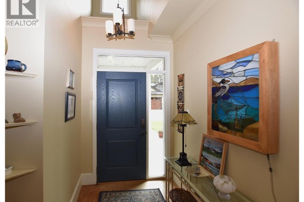 Interior entryway with a dark blue front door, light yellow walls, decorative art, and a console table. - 430 Hummingbird Avenue, Vernon