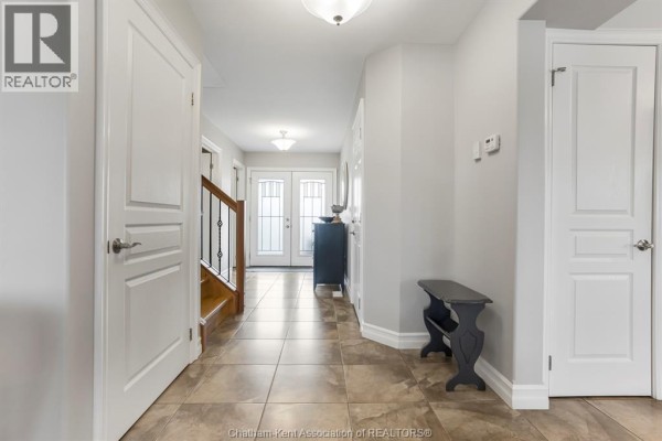 Interior foyer with tan tiled floor, dark dresser, staircase with black railings, and a view of the living room. - 430 Twilight Trail, Chatham