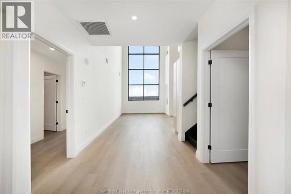 Interior hallway with white walls, light wood flooring, and a large geometric window. - 4300 Laurier Parkway Unit# 624, Lasalle
