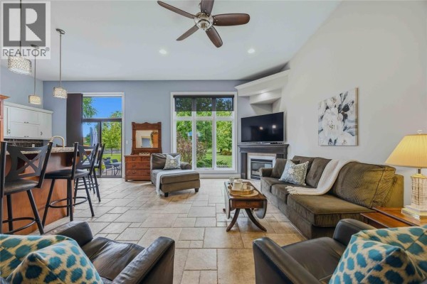 Open-concept living area with a kitchen island, bar stools, sofas, fireplace, and large windows. - 4303 Garden Crescent, Petrolia