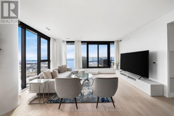 Living area with a light wood floor, white sofa, two grey accent chairs, and floor-to-ceiling windows with city views. - 4304 - 16 Bonnycastle Street, Toronto