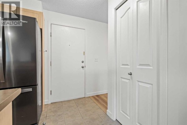 Interior entryway with beige tile flooring, a white door, and a stainless steel refrigerator. - 4307, 60 Panatella Street Nw, Calgary