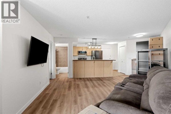 Open concept living space with hardwood floors, a kitchen island, and a doorway to a bathroom. - 4307, 60 Panatella Street Nw, Calgary