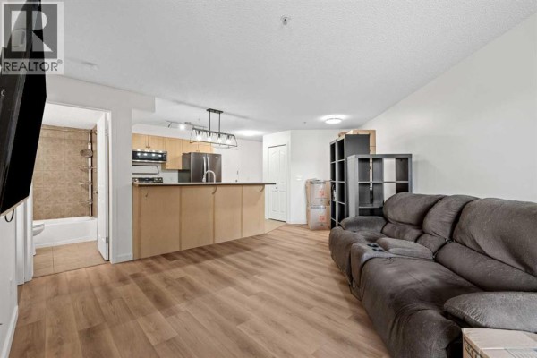 Living area with a sofa, kitchen island, and view into the bathroom with a shower. - 4307, 60 Panatella Street Nw, Calgary