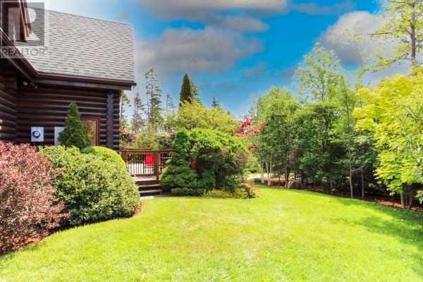 Lush green lawn and mature trees surrounding the log cabin exterior. - 431-435 Dogberry Hill Road, Portugal Cove St  Philips