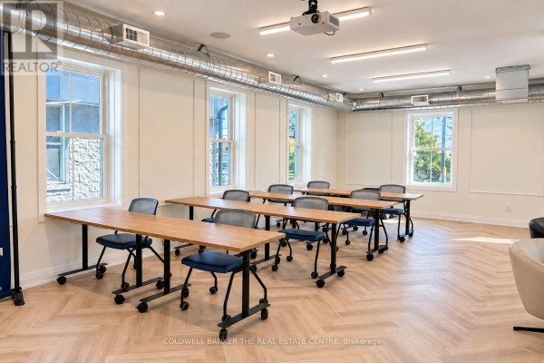Meeting room with multiple work tables, chairs, large windows, and exposed ductwork. - 431 Davis Drive, Newmarket