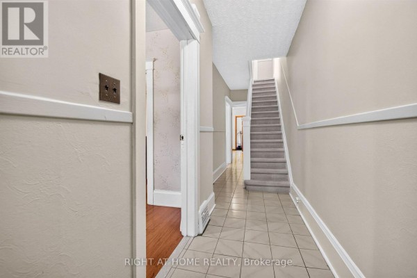 Interior hallway with tiled floor, beige walls, and a carpeted staircase. - 431 Lansdowne Avenue, Toronto
