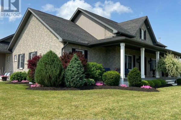 Exterior of a stone-clad house with a covered porch, manicured shrubs, and green lawn. - 431 Meadowview Road, Kawartha Lakes