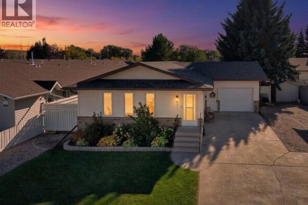 Front exterior of a white and brick bungalow at dusk with illuminated windows and a colourful sky. - 431 Peters Street, Warman