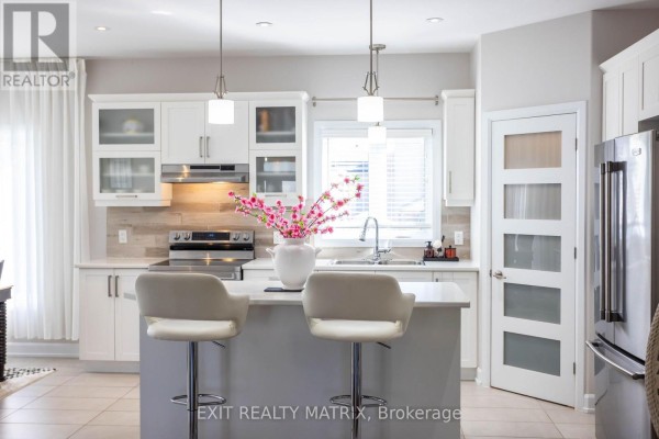 White kitchen with stainless steel appliances, quartz countertops, island with two stools, and pendant lights. - 431 Provence Avenue, Russell