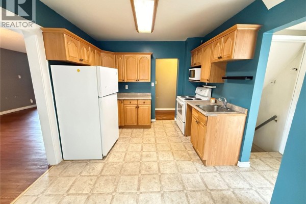 Kitchen with light wood cabinets, white appliances, and teal walls, showing a doorway to a hallway. - 431 Qu'appelle Street, Weyburn