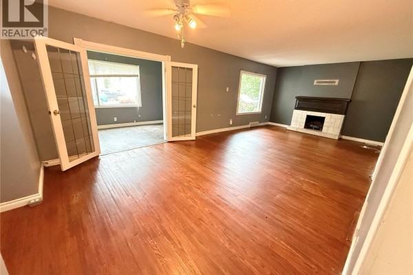 Living room with hardwood floors, gray walls, a fireplace, and glass-paneled doors opening to another room. - 431 Qu'appelle Street, Weyburn