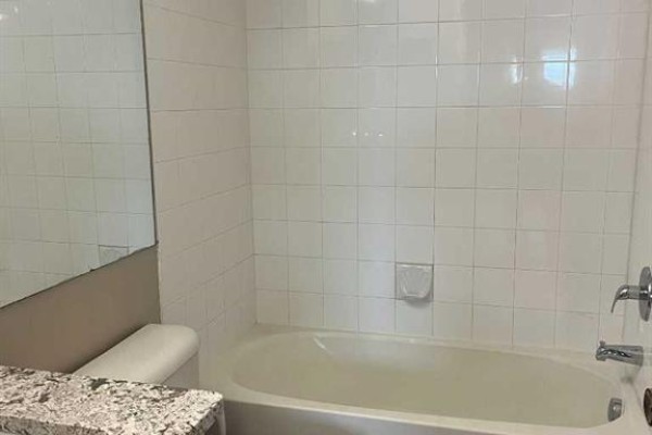 Empty room with light brown walls, wood-look laminate flooring, and a large window. - 4312, 4975 130 Avenue Se, Calgary
