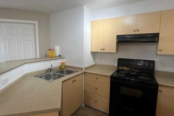 Empty room with light brown walls, wood-look laminate flooring, and a large window. - 4312, 4975 130 Avenue Se, Calgary