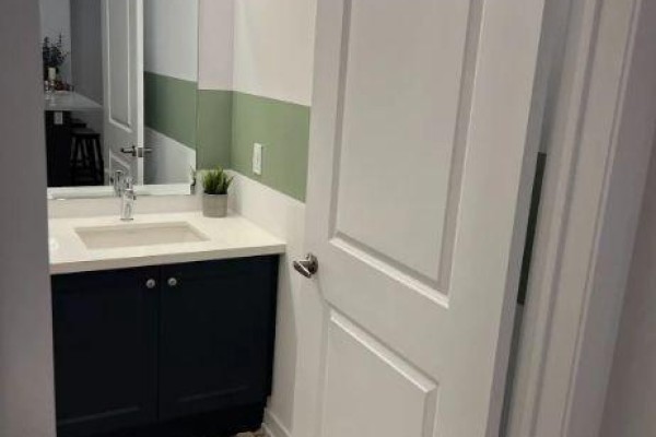 Powder room with a dark blue vanity, white countertop, and mirror reflecting a kitchen island. - 432 - 10 Mallard Trail, Hamilton