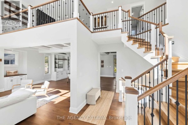 Spacious entryway with a grand staircase, wood flooring, white walls, and a view into the living area. - 432 Ashbee Court, Ottawa
