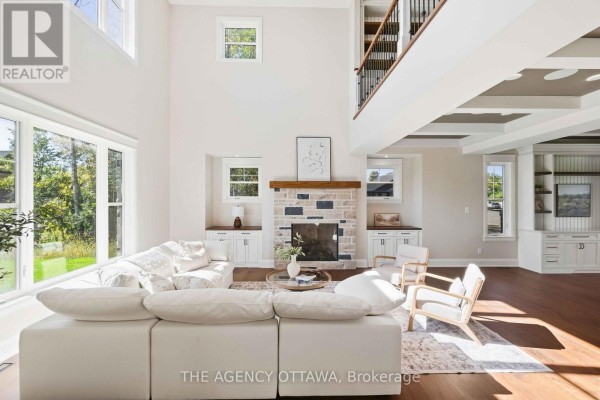 Living room with a high ceiling, large windows, a stone fireplace, white sectional sofa, and built-in shelving. - 432 Ashbee Court, Ottawa