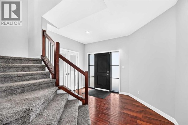 Interior foyer with gray walls, hardwood floors, carpeted stairs, and a black front door. - 432 Sixmile Cove S, Lethbridge