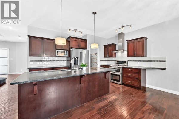 Kitchen with dark wood cabinets, granite island, stainless steel appliances, and white tile backsplash. - 432 Sixmile Cove S, Lethbridge