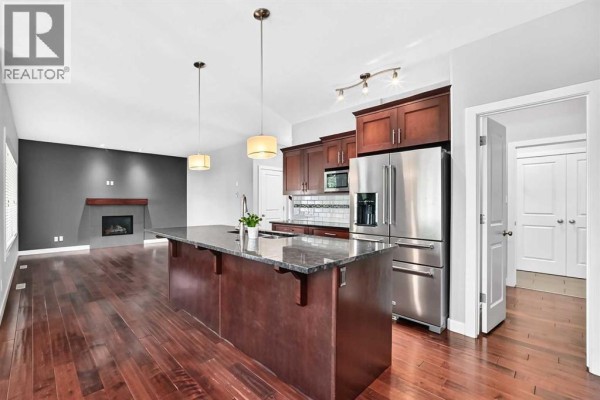 Open-concept kitchen and living room with a fireplace and dark hardwood floors. - 432 Sixmile Cove S, Lethbridge
