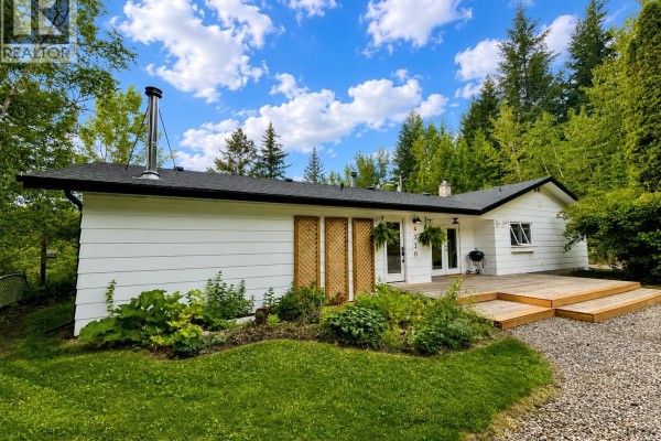 Exterior view of the white house showing a wooden deck and garden beds. - 4320 Quesnel-hixon Road, Quesnel