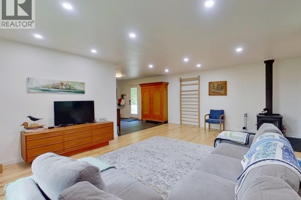 Living room with a large sectional sofa, television, wood buffet, and wood-burning stove. - 4320 Quesnel-hixon Road, Quesnel