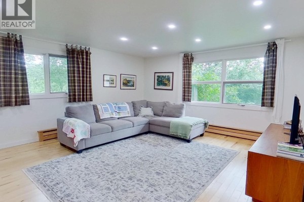 Living room with a grey sectional sofa, large area rug, and large windows. - 4320 Quesnel-hixon Road, Quesnel