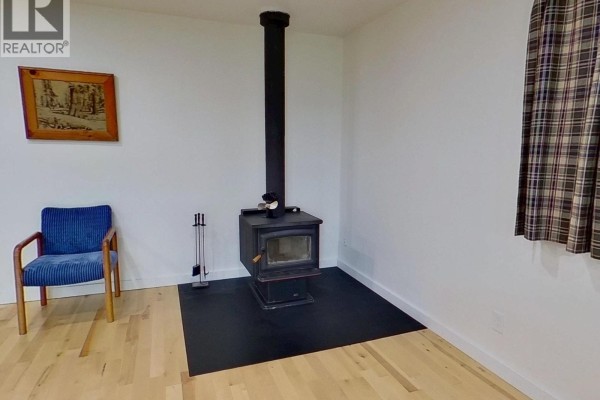 Close-up of a wood-burning stove in a white room with a blue chair. - 4320 Quesnel-hixon Road, Quesnel