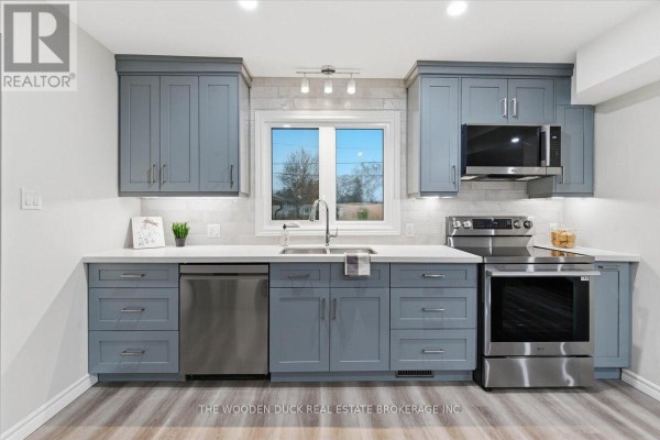 A modern kitchen featuring grey cabinets, white countertops, stainless steel appliances, and a window above the sink. - 4329 Old Hwy 2 Highway, Belleville