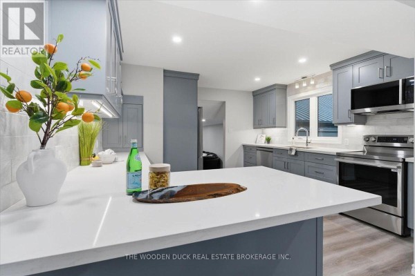 A kitchen with grey cabinets, white countertops, stainless steel appliances, and a view of the staircase. - 4329 Old Hwy 2 Highway, Belleville