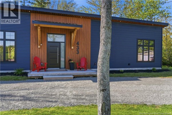 Front exterior of a modern house with blue siding, wood accents, and a gravel driveway. - 433 Cornwall Road, Shediac