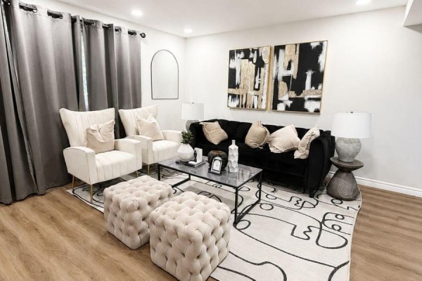 Living room with black and cream furniture, abstract art, and two tufted ottomans. - 433a Dunvegan Drive, Waterloo