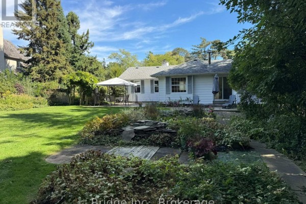 View of the backyard with a patio, lawn, garden beds, and mature trees. - 434 Apple Lane, Mississauga