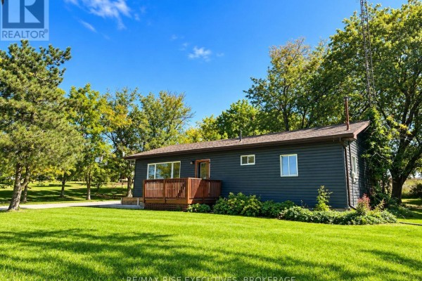 Rear view of the bungalow with a wooden pergola over a deck and green backyard. - 434 County Rd 9, Greater Napanee