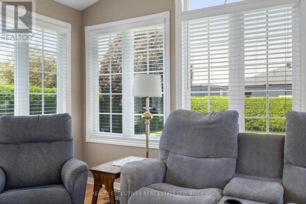 Close-up view of grey recliners in a sunroom with large windows showing green trees and foliage. - 434 Queen Street, North Dundas