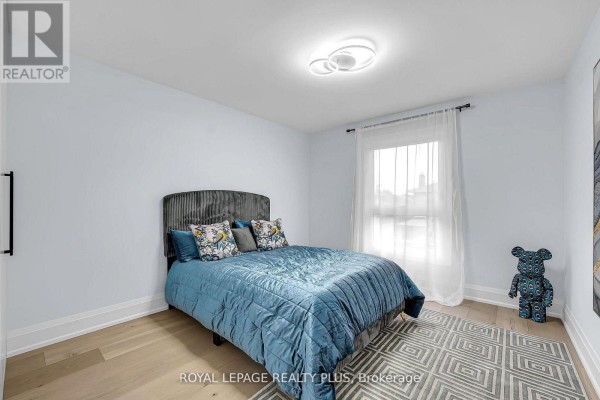 Bedroom with a grey upholstered headboard, blue bedding, a patterned rug, and light wood floors. - 4344 Dallas Court, Mississauga