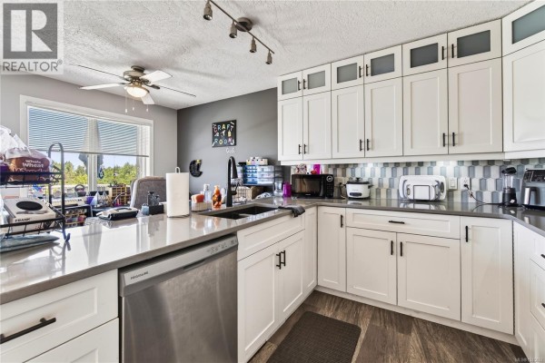 Kitchen with white cabinets, grey countertops, stainless steel sink, and a large window overlooking the yard. - 4346 Gulfview Dr, Nanaimo