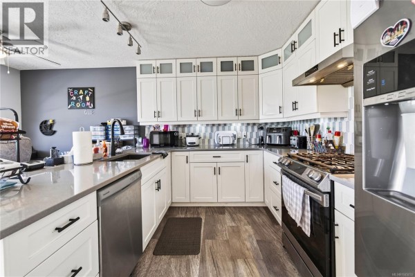 Kitchen with white cabinets, grey quartz countertops, a stainless steel range, and a modern backsplash. - 4346 Gulfview Dr, Nanaimo