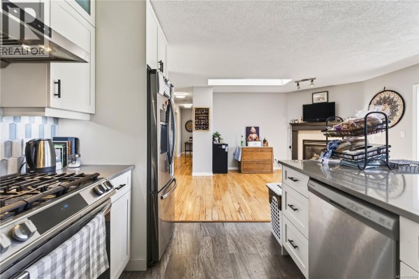 View from the kitchen into a living area with hardwood floors, a fireplace, and a skylight. - 4346 Gulfview Dr, Nanaimo