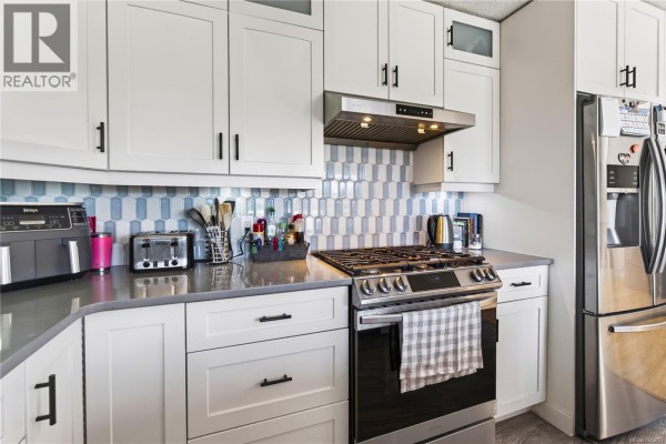 Close-up of the kitchen featuring white cabinets, a gas range, stainless steel refrigerator, and decorative backsplash. - 4346 Gulfview Dr, Nanaimo