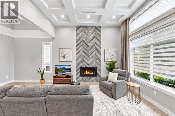 Living room with grey seating, a fireplace with a wood-look tile surround, and large windows. - 4348 Carleton Avenue, Burnaby