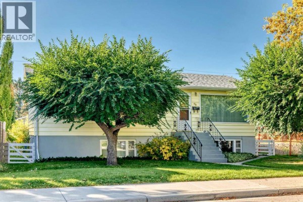 Front exterior of a yellow house with white trim and a large tree in the yard. - 435 51 Avenue, Calgary