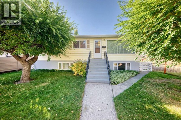 Front exterior of a yellow house with a concrete walkway and stairs to the entrance. - 435 51 Avenue, Calgary