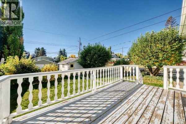 Wooden deck with white railings overlooking a grassy backyard and trees. - 435 51 Avenue, Calgary