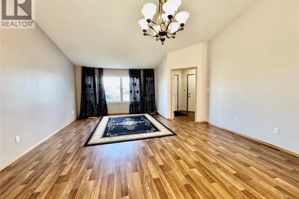 Living room with wood laminate flooring, a large dark rug, and decorative curtains. - 435 Southwood Drive, Prince Albert