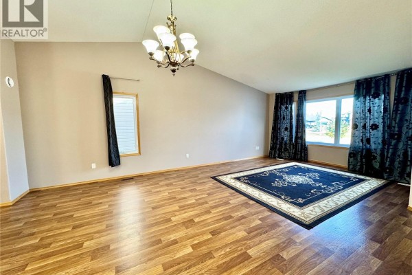 Spacious living room featuring vaulted ceiling, wood laminate floors, and large window with curtains. - 435 Southwood Drive, Prince Albert