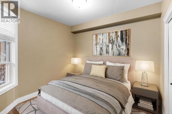 Bedroom with a queen bed, side tables, and artwork on a tan wall. - 4350 Ponderosa Drive Unit# 108, Peachland