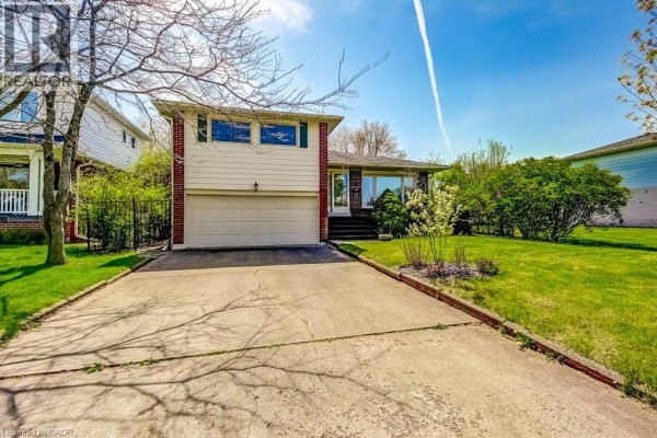 Concrete driveway leading to a beige siding and red brick house with white garage door. - 4356 Dublin Crescent, Burlington