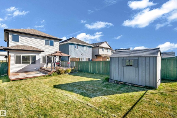 Backyard view with a wooden deck, gazebo, shed, and green lawn surrounded by a fence. - 4359 126 Av Nw, Edmonton