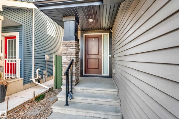 Front entrance with concrete steps, a brown door, stone pillar, and beige siding. - 4359 126 Av Nw, Edmonton